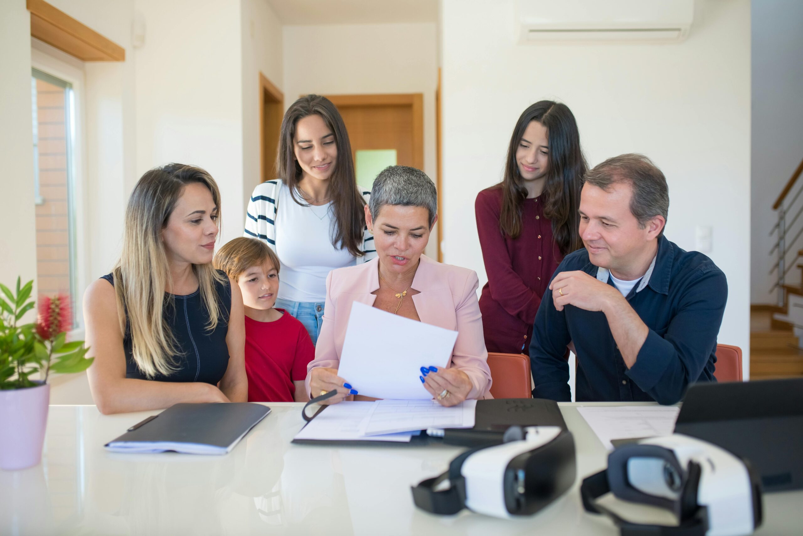 Confident woman in a pink blazer and a document, smiling indoors with a family.